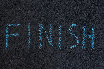 Text FINISH underfoot. Black asphalt with chalk inscription. The end concept