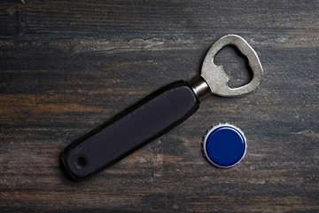 Bottle opener beside a bottle cap  lying on a wooden table. High angle view with copy space.  