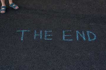 Text THE END underfoot. Feet and inscription on asphalt. Notice on road.