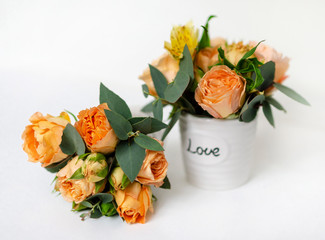 flower arrangement of orange roses and green leaves of eucalyptus in a vintage pot on a white...