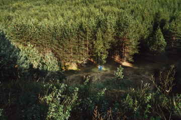 The boy stands at the pine forest. View from the top.