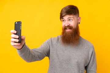 Redhead man with long beard over isolated yellow background making a selfie