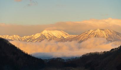 Aerial view of snowy mountain hills with morning mist or fog at sunrise in Nagano City, Japan....