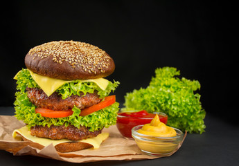 Ready-made hamburger with beef cutlets, cheese, cucumber, fresh tomatoes and salad on a dark background. Fast food. Cooking. Copy space. Place for text.