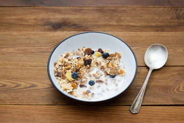 Whole oats breakfast, granola with dried fruit and blueberry, milk and honey. Wooden background. Copy space.