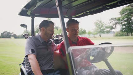 Two Mature Male Golfers In Golf Buggy On Fairway Discussing Scorecard