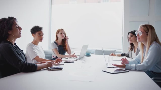 Team Of Young Businesswomen With Laptops And Tablets Meeting Around Table In Modern Workspace