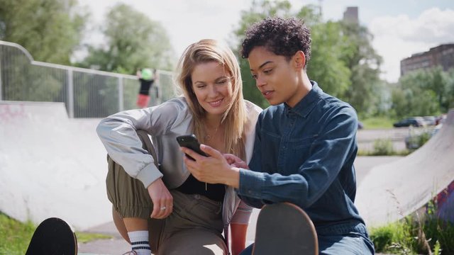 Two Female Friends Looking At Mobile Phone In Urban Skate Park And Laughing