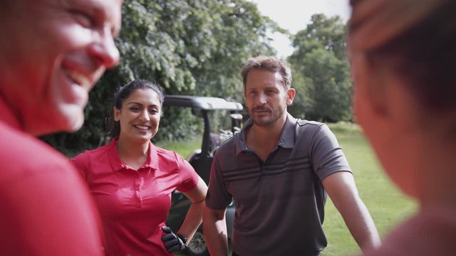 Group Of Male And Female Golfers Standing By Golf Buggy On Course Talking Together
