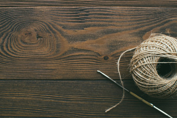 Crochet hook and jute thread ball at wooden background. Eco-friendly knitting.