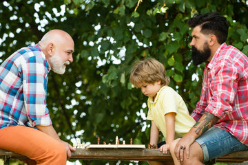 Fathers day. Old man with little boy playing chess. Father and Grandfather with son playing Chess in the park at the day time.