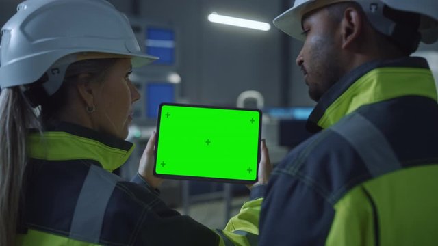 Industry 4.0 Factory: Chief Engineer and Project Supervisor in Safety Vests and Hard Hats, Talk, Use Digital Tablet Computer with Green Screen, Chroma Key. Workshop with Machinery. Zoom Out