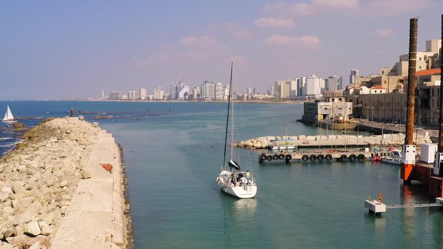 Small boat leaving the old city port of Jaffa with Tel Aviv skyline in the background, low flight aerial view.