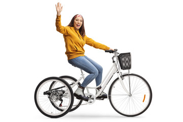 Cheerful young female riding a tricycle and waving at the camera