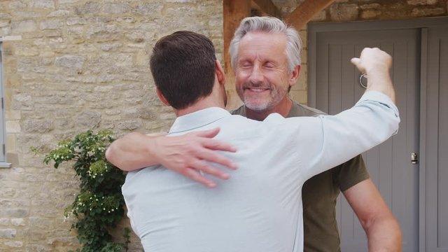 Senior Father Greets And Hugs Adult Son Outside Front Door Of House As He Visits