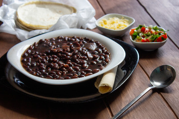 Plato de frijoles negros con salsa mexicana tortillas y queso cotija en mesa de madera