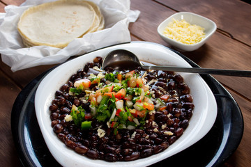 Plato de frijoles cocidos con tortillas y salsa mexicana quesillo en mesa de madera