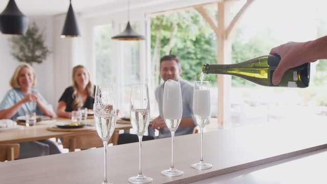 Senior Man Opens Bottle Of Champagne As Family With Adult Offspring Eat Meal Around Table At Home 