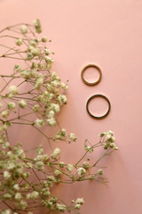 Two gold wedding rings and gypsophila flowers on pale pink background. Top view.