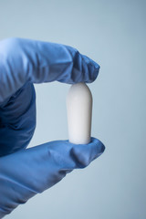 A doctor’s hand in a glove holds a vaginal rectal anal suppository. Candle from hemorrhoids, pain, fever, thrush, vaginitis, inflammation, constipation, infections.