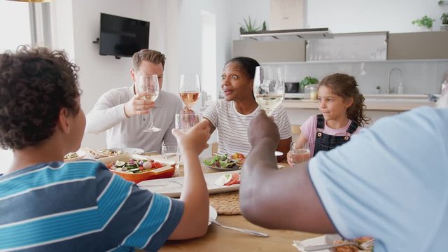 Multi-Generation Mixed Race Family Making A Toast Before Eating Meal Around Table At Home Together
