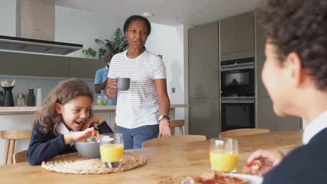 Grandparents Sitting In Kitchen With Grandchildren Eating Breakfast Before Going To School