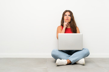 Young woman with a laptop sitting on the floor thinking an idea