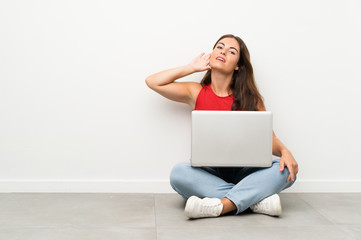 Young woman with a laptop sitting on the floor listening something