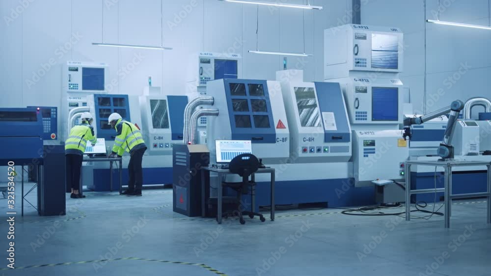Poster Chief Engineer and Project Manager Wearing Safety Vests and Hard Hats Work on Compute, Talk, Optimize Production Line. On Foreground: industry 4.0 Modern Factory with CNC Machinery and robot arm
