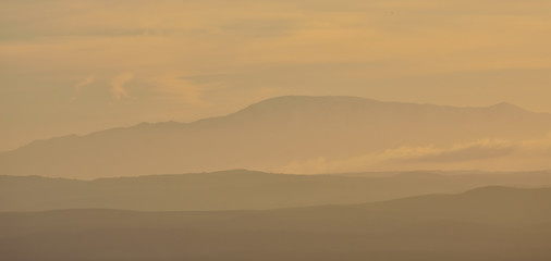 Silhouette of distant mountains between mist at sunset