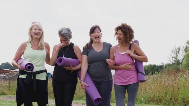 Group Of Mature Female Friends On Outdoor Yoga Retreat Walking Along Path Through Campsite