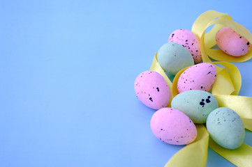 Fototapeta na wymiar Close up easter composition, pink green quail eggs with yellow ribbon on pastel blue background. Copy space for text. View from the top.