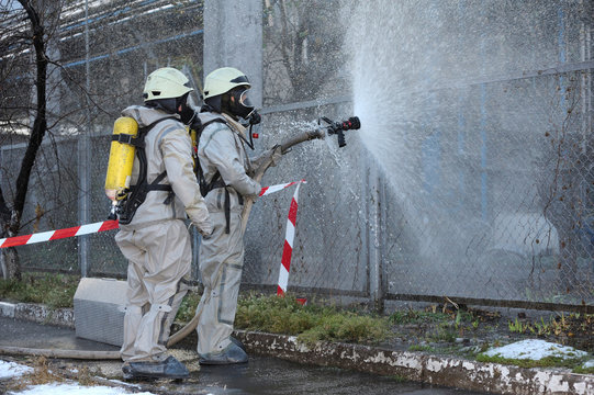 Rescuers in protective rubber suits watering plant territory with syringe. Rescue team training in decontamination