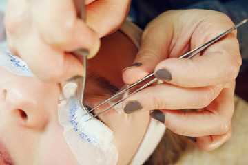 Obraz na płótnie Canvas Close up on the hands of the beautician Eyelash Extension Procedure Woman Eye making artificial Long Eyelashes in a beauty salon