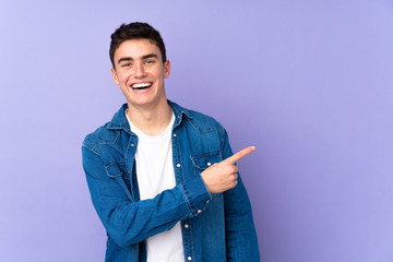 Teenager caucasian  handsome man isolated on purple background surprised and pointing side