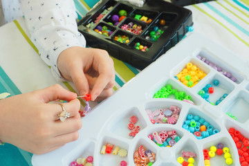 .plastic substrates with multi-colored beads and the hands of a girl making a bracelet. handmade,...