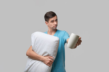 Young brunet man holding white cup of coffee and white pillow