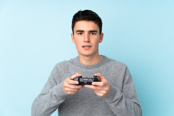 Teenager caucasian man playing with a video game controller isolated on blue background