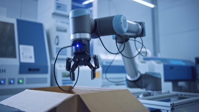 Industry 4.0 Modern Factory: Programmed robot arm Packing Metal Components into Cardboard Box. Assembly Line Machine Picks and Packs Product into Package on Conveyor. Fully Automated Warehouse Robotic