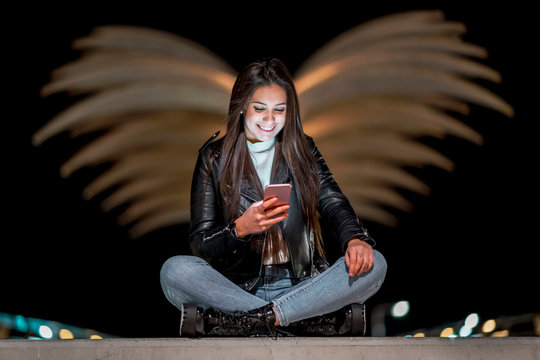 Portrait of happy teenage girl looking at smartphone at night