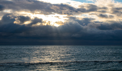 blue dark stormy clouds above the sea, the sun rays breaks through the clouds