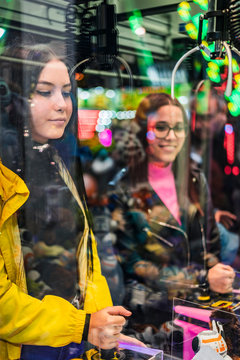 Two teenage girls playing at a fairground booth on a funfair at night
