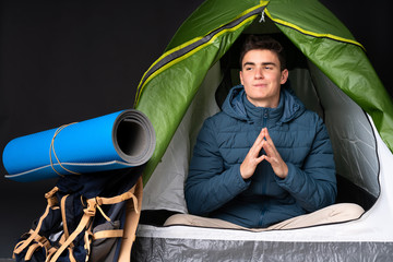 Teenager caucasian man inside a camping green tent isolated on black background scheming something