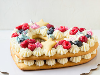 Tasty heart-shaped cake with fresh berries on a white background.