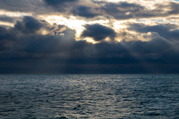 Fototapeta na wymiar blue dark stormy clouds above the sea, the sun rays breaks through the clouds