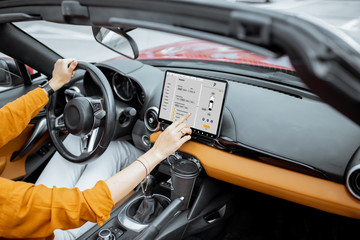 Cheerful woman controlling car with a digital dashboard, switching autopilot mode while driving a...