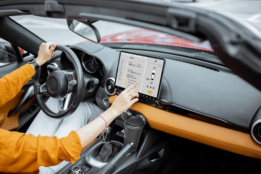 Cheerful woman controlling car with a digital dashboard, switching autopilot mode while driving a cabriolet. Smart car concept
