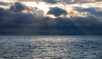 blue dark stormy clouds above the sea, the sun rays breaks through the clouds