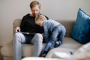 Father and son looking at book on couch at home
