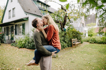Happy couple kissing in garden, in front of their dream house